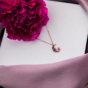 A sterling silver pendant chain with a black moon motif, displayed on a white box with a pink flower beside it.